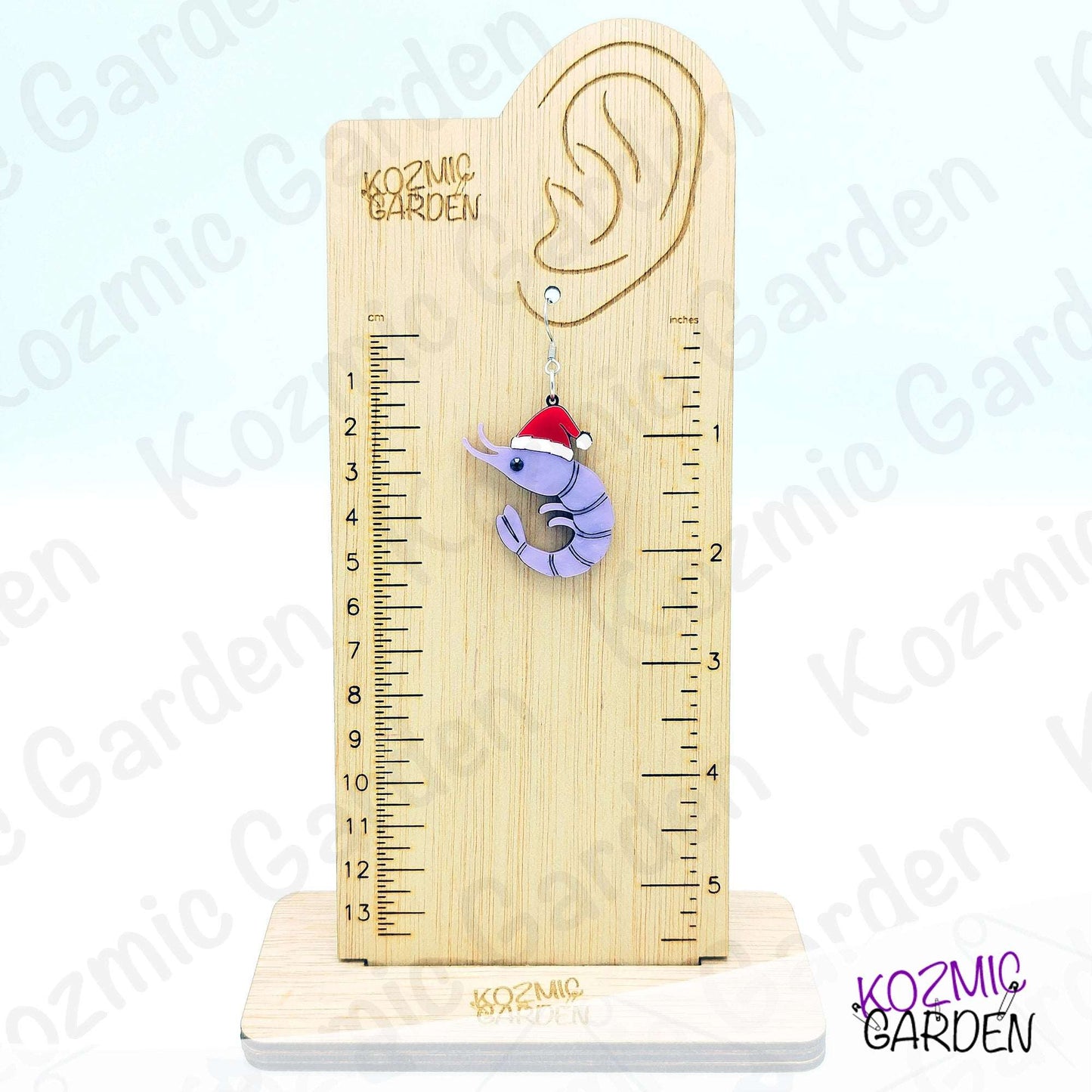 Wooden ear gauge with a ruler and a purple earring shaped like a shrimp with a Santa hat on a white background.