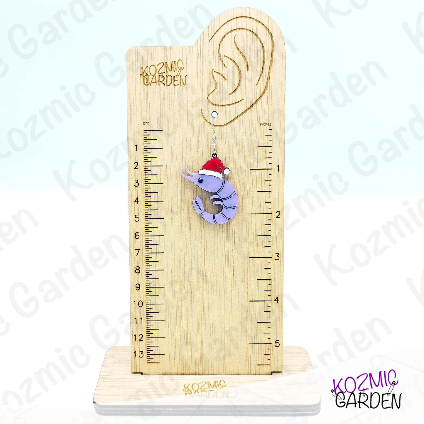 Wooden ear gauge with a ruler and a purple earring shaped like a shrimp with a Santa hat on a white background.