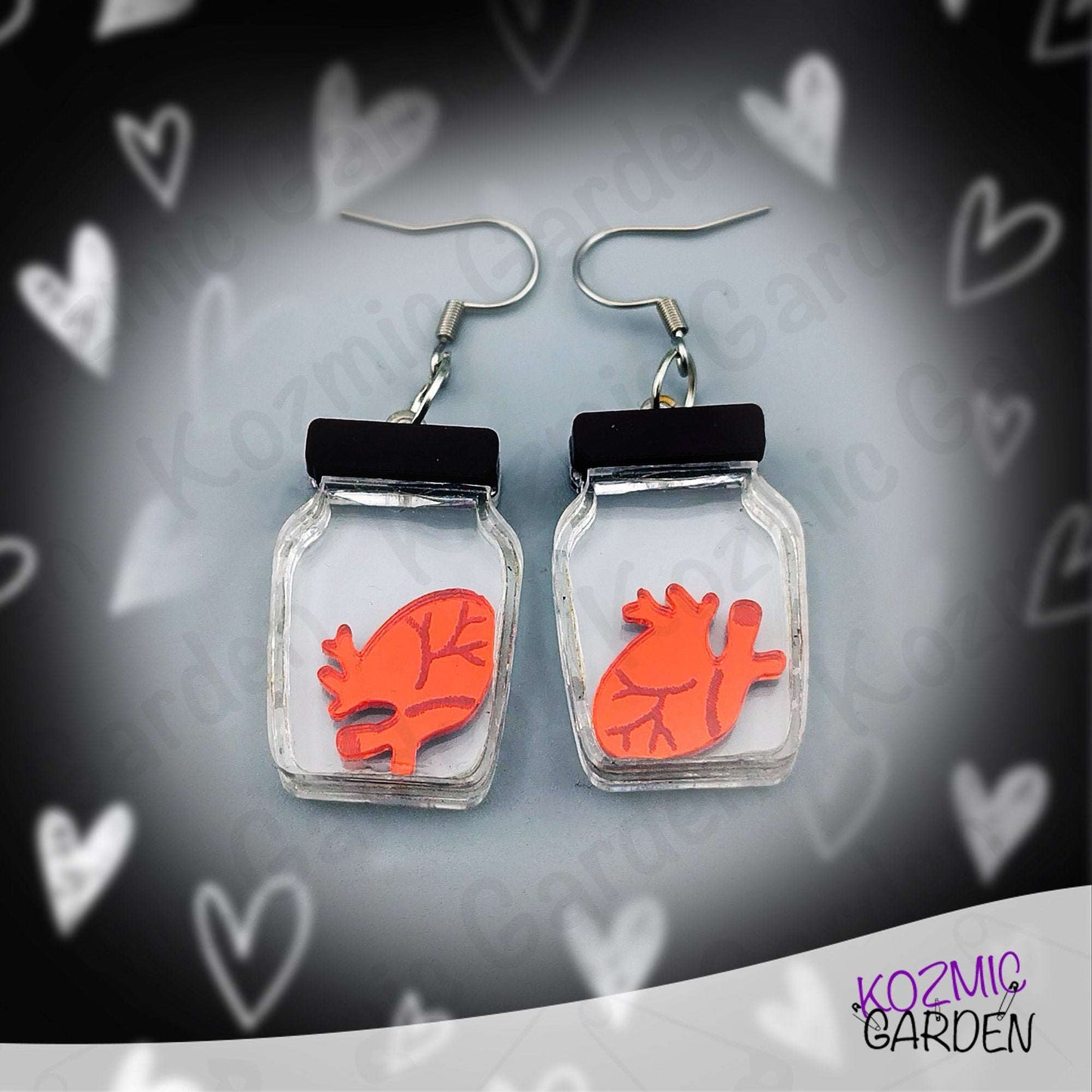 Earrings with red heart design in clear jars on a heart-patterned background, branded 'Kozmic Garden'.