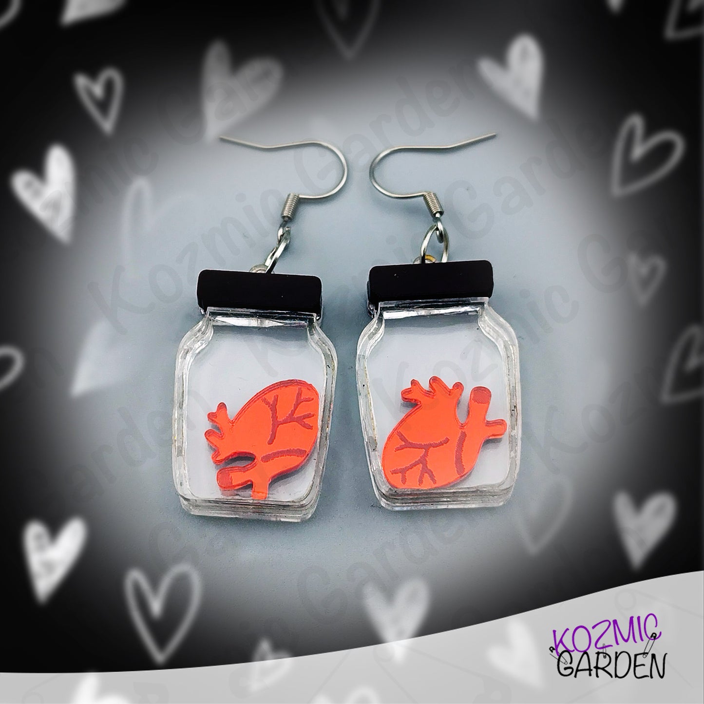 Earrings with red heart design in clear jars on a heart-patterned background, branded 'Kozmic Garden'.