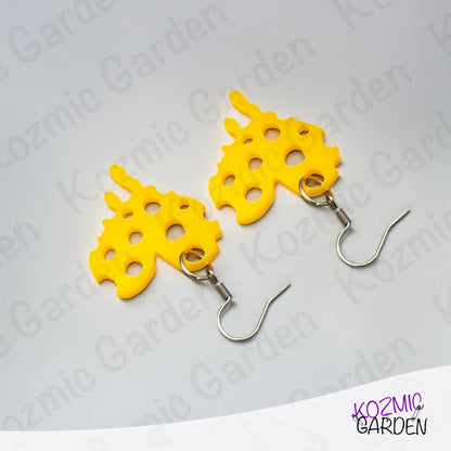 Yellow earrings with unique design of cheese heart on a gray background with 'Kozmic Garden' branding.