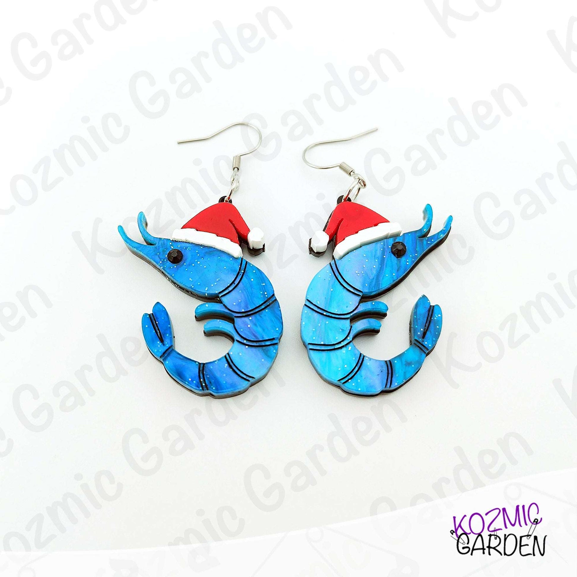Blue shrimp earrings with red Santa hats on a white background with 'Kozmic Garden' branding.