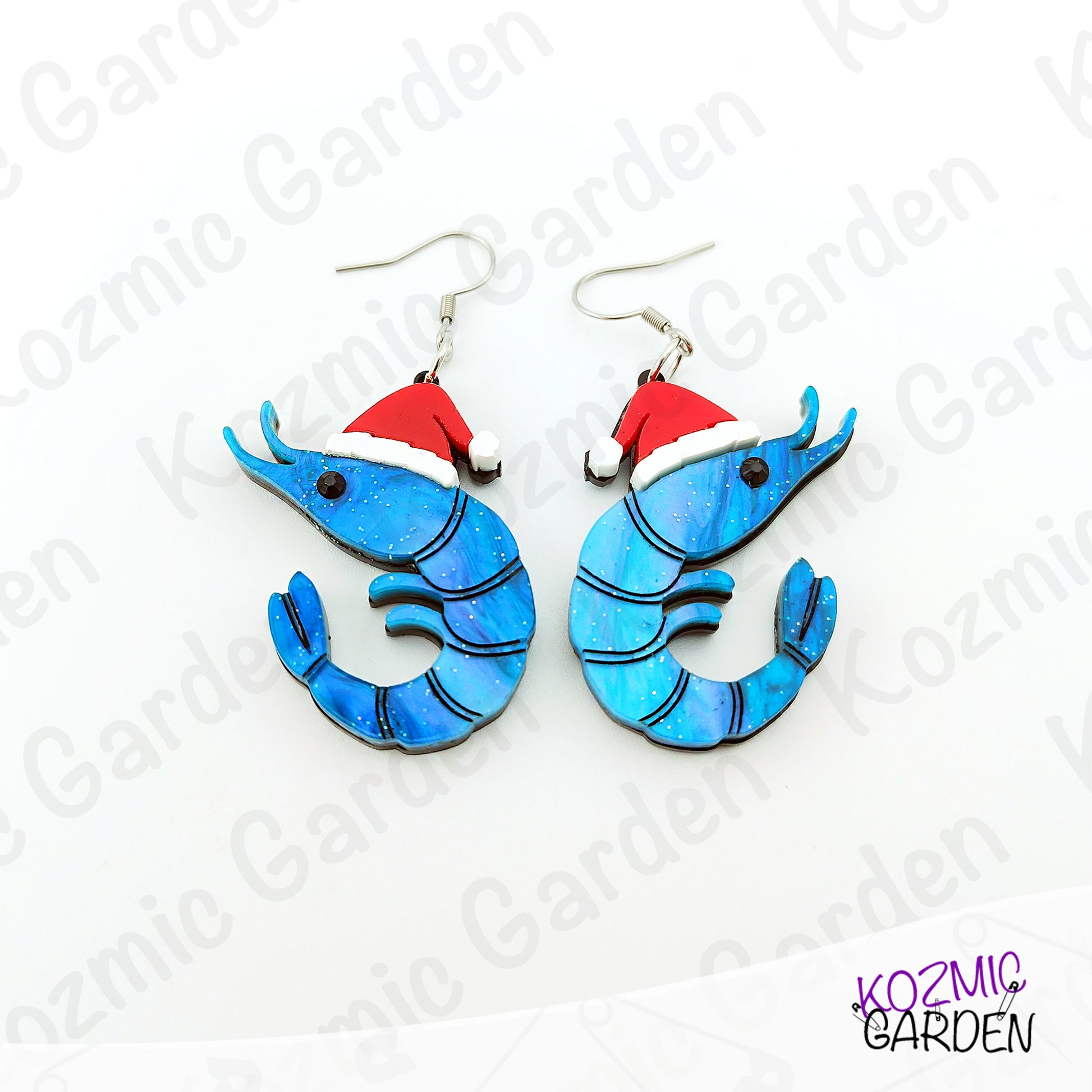 Blue shrimp earrings with red Santa hats on a white background with 'Kozmic Garden' branding.