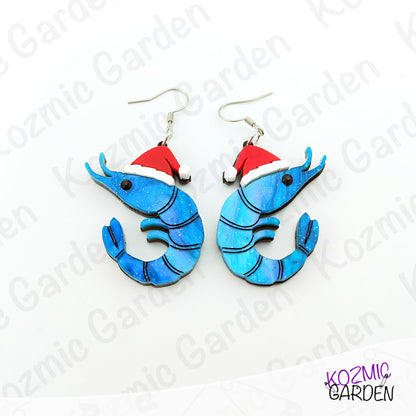 Blue shrimp earrings with red Santa hats on a white background with 'Kozmic Garden' branding.
