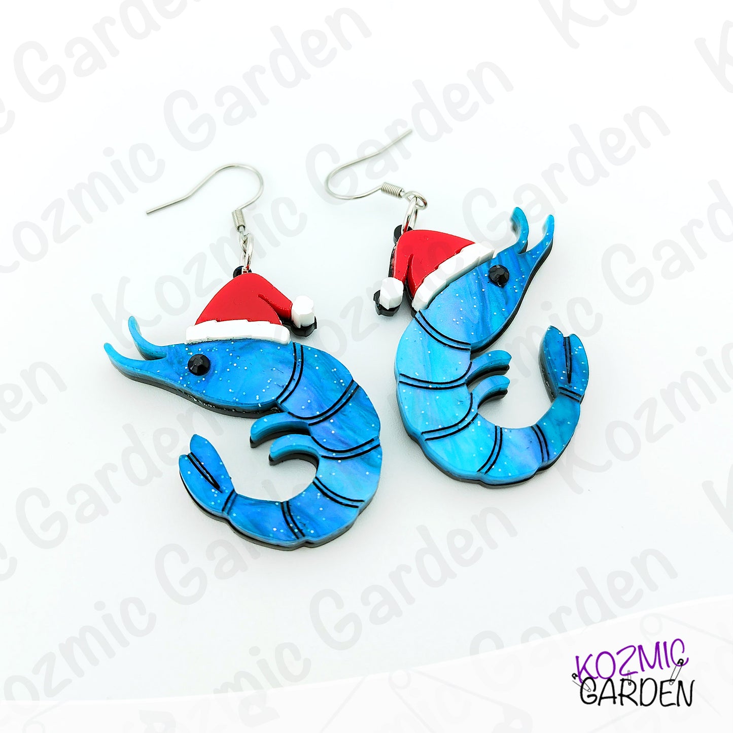 Blue shrimp earrings with red Santa hats on a white background with 'Kozmic Garden' branding.