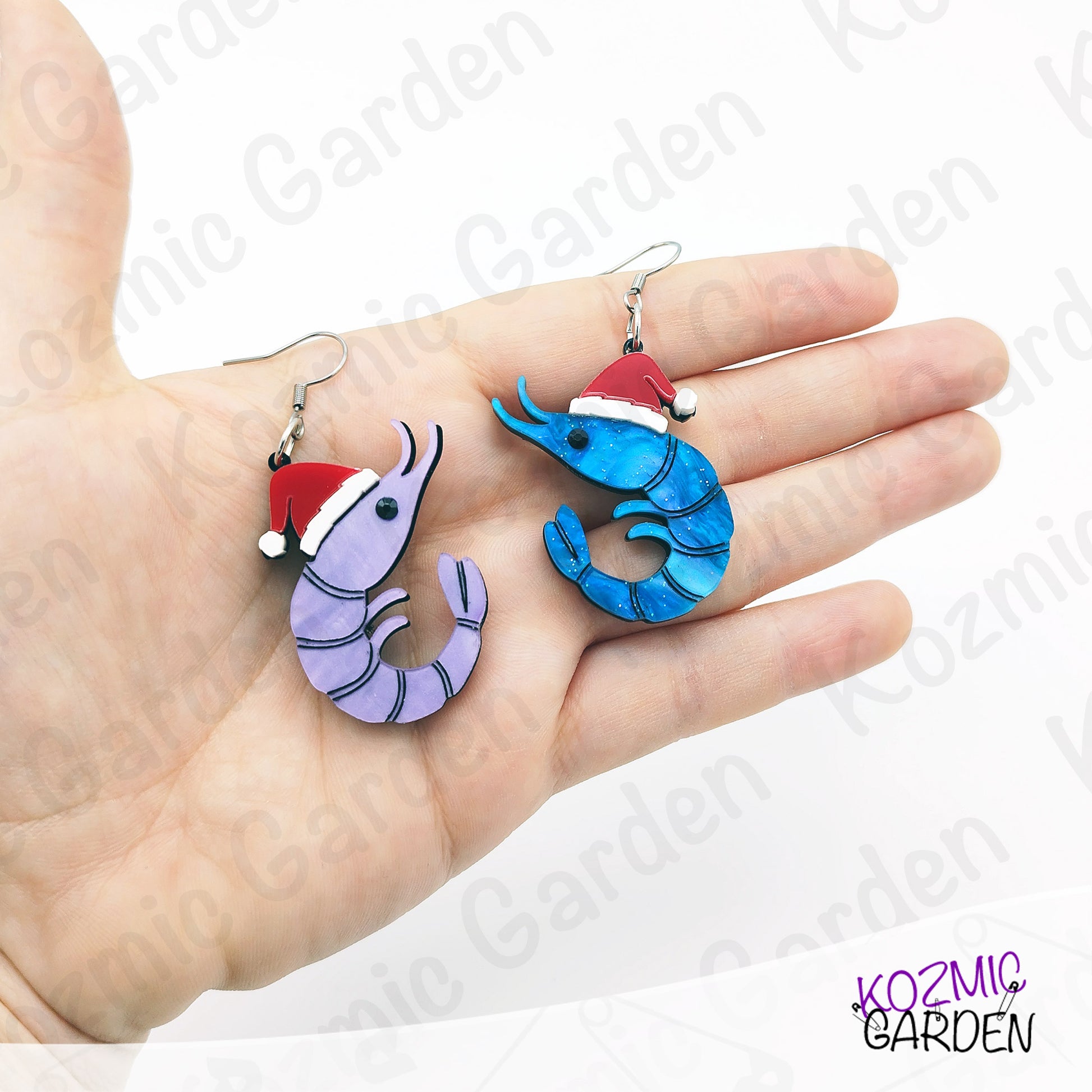 Hand holding two novelty earrings shaped like shrimps with Santa hats on a white background.
