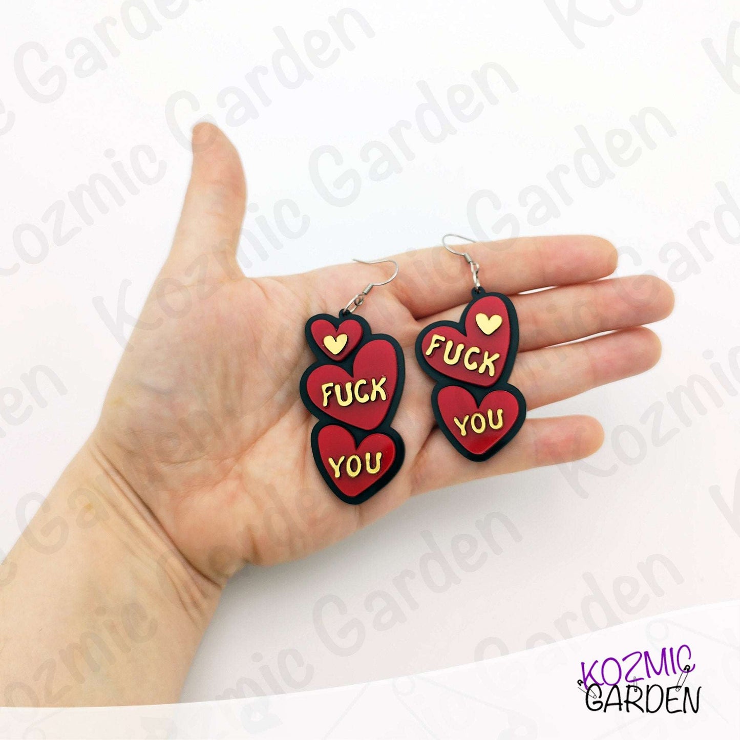 Heart-shaped earrings with text held in a hand, brand 'Kozmic Garden' visible