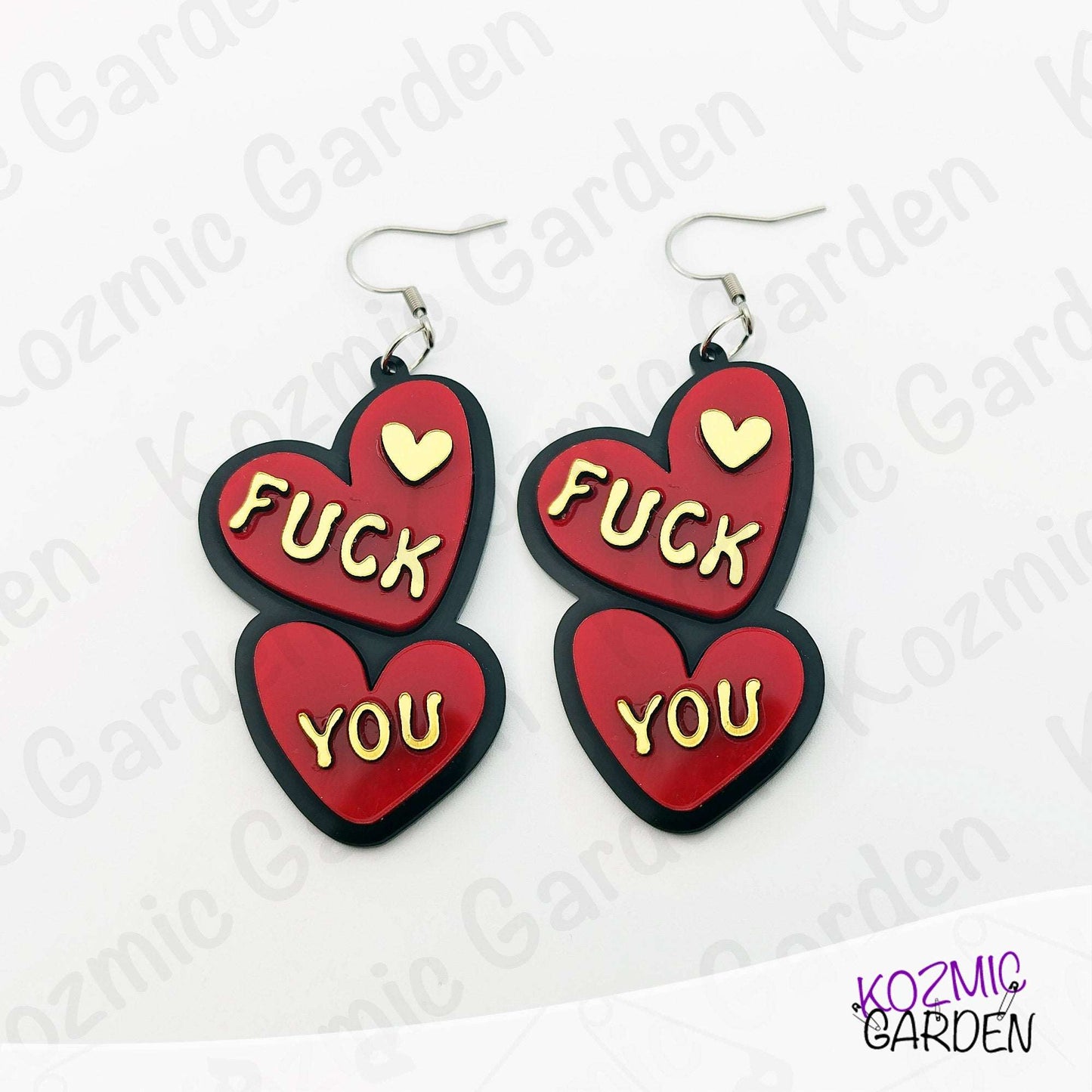 Red heart-shaped earrings with 'FUCK YOU' text on a white background with 'Kozmic Garden' branding.