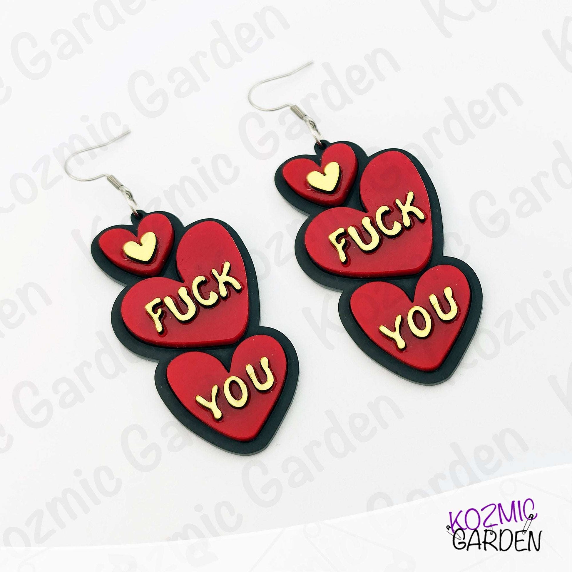 Red heart-shaped earrings with 'FUCK YOU' text on a white background with 'Kozmic Garden' branding.