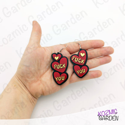 Heart-shaped earrings with text held in a hand, brand 'Kozmic Garden' visible