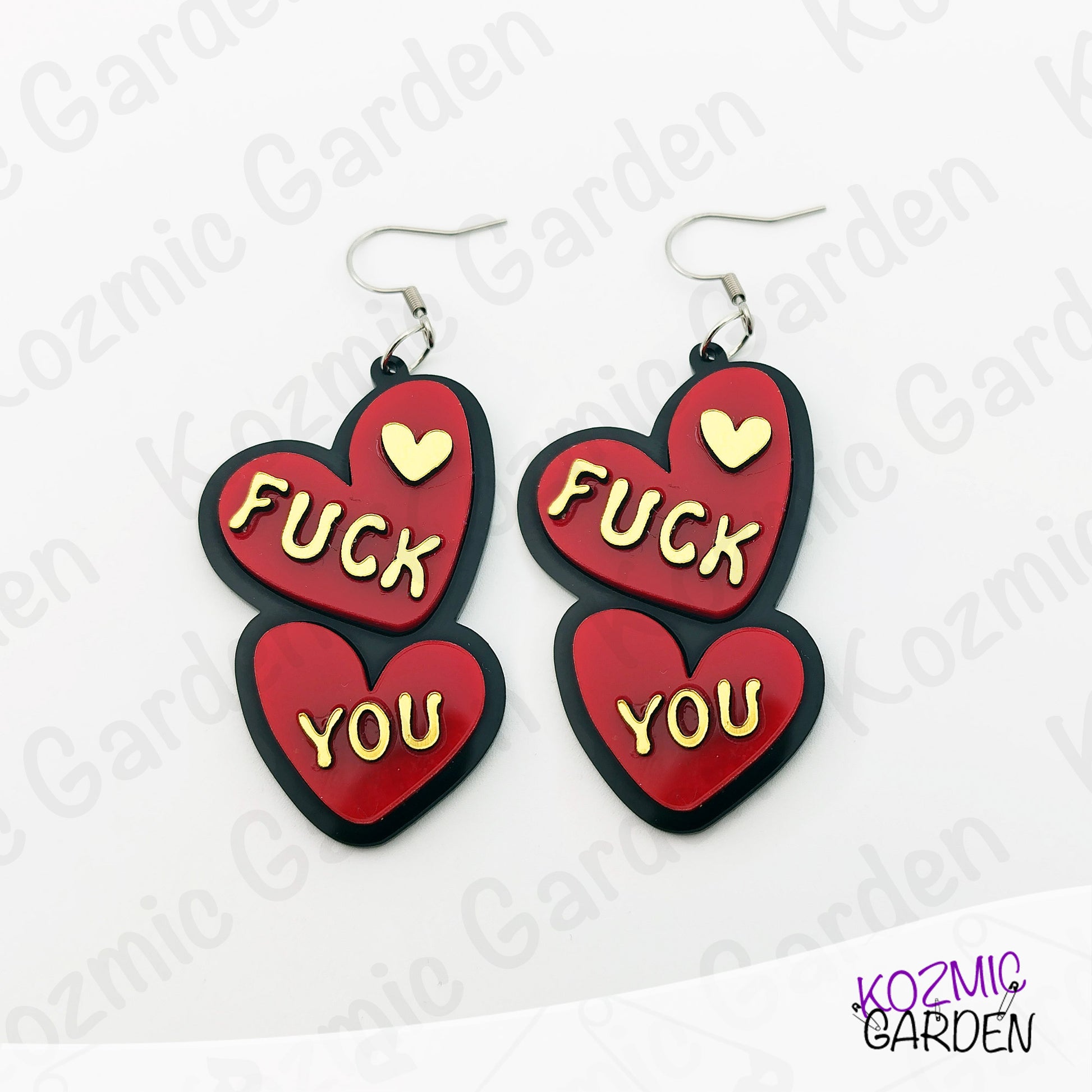 Red heart-shaped earrings with 'FUCK YOU' text on a white background with 'Kozmic Garden' branding.