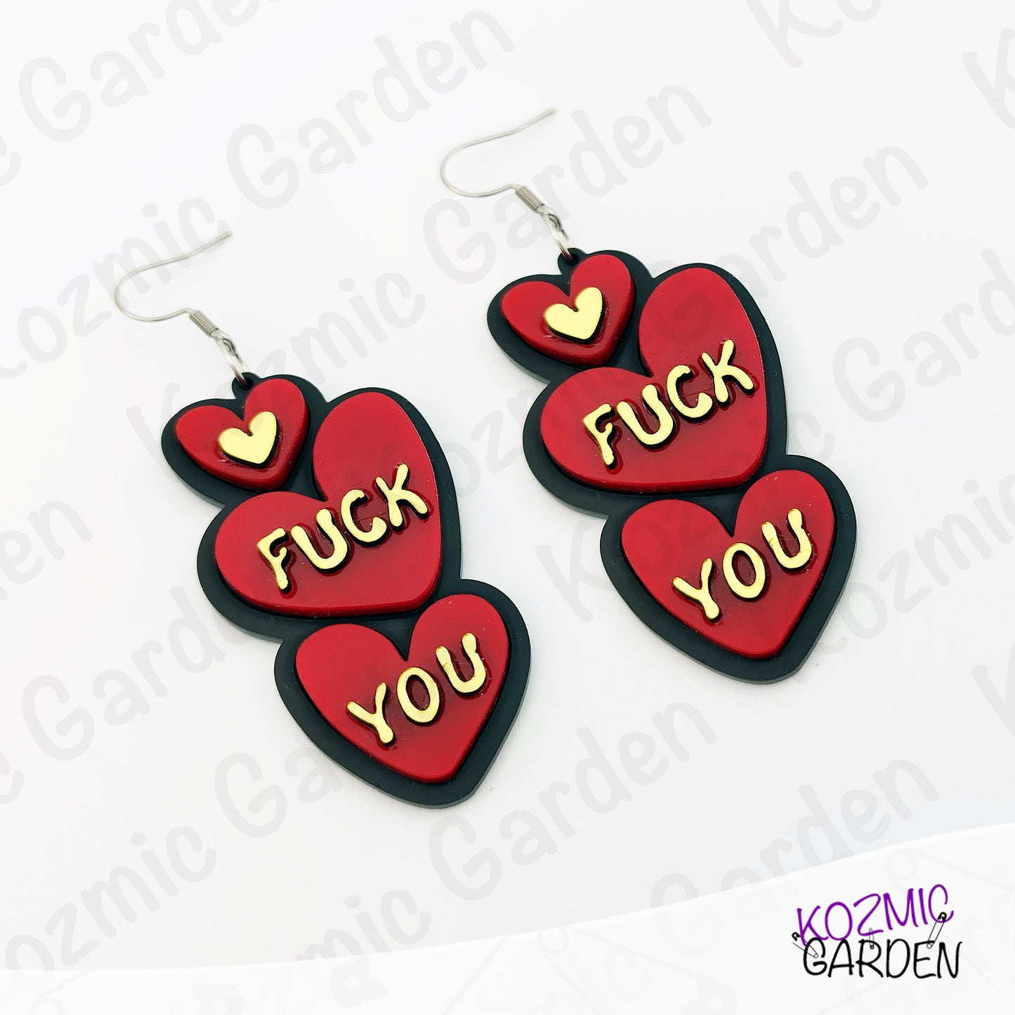 Red heart-shaped earrings with 'FUCK YOU' text on a white background with 'Kozmic Garden' branding.