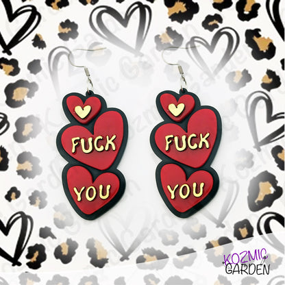 Earrings with red hearts and gold text "Fuck You"  on a patterned background