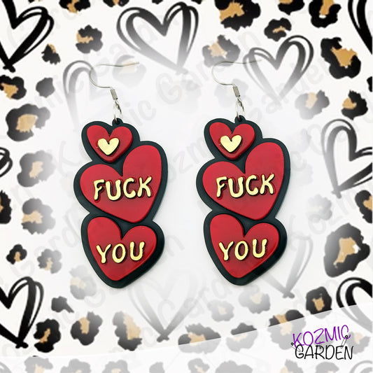 Earrings with red hearts and gold text "Fuck You"  on a patterned background
