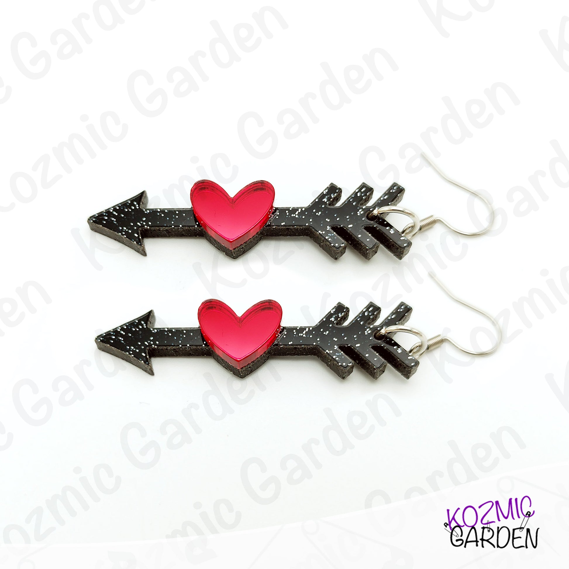 Pair of arrow-shaped earrings with red hearts on a white background, branded 'Kozmic Garden'.