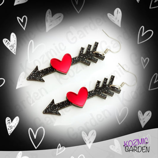 Pair of arrow-shaped earrings with red hearts on a black background with heart designs.
