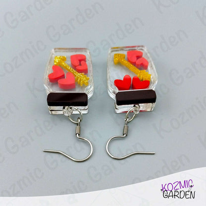 Pair of earrings with heart and key design on a gray background, branded 'Kozmic Garden'.