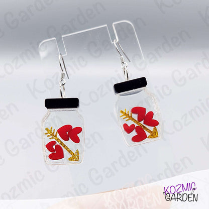 Jar-shaped earrings with red heart and arrow design on a gray background, branded 'Kozmic Garden'.