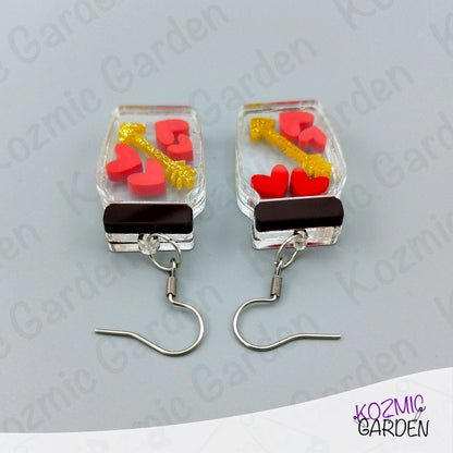 Pair of earrings with heart and key design on a gray background, branded 'Kozmic Garden'.