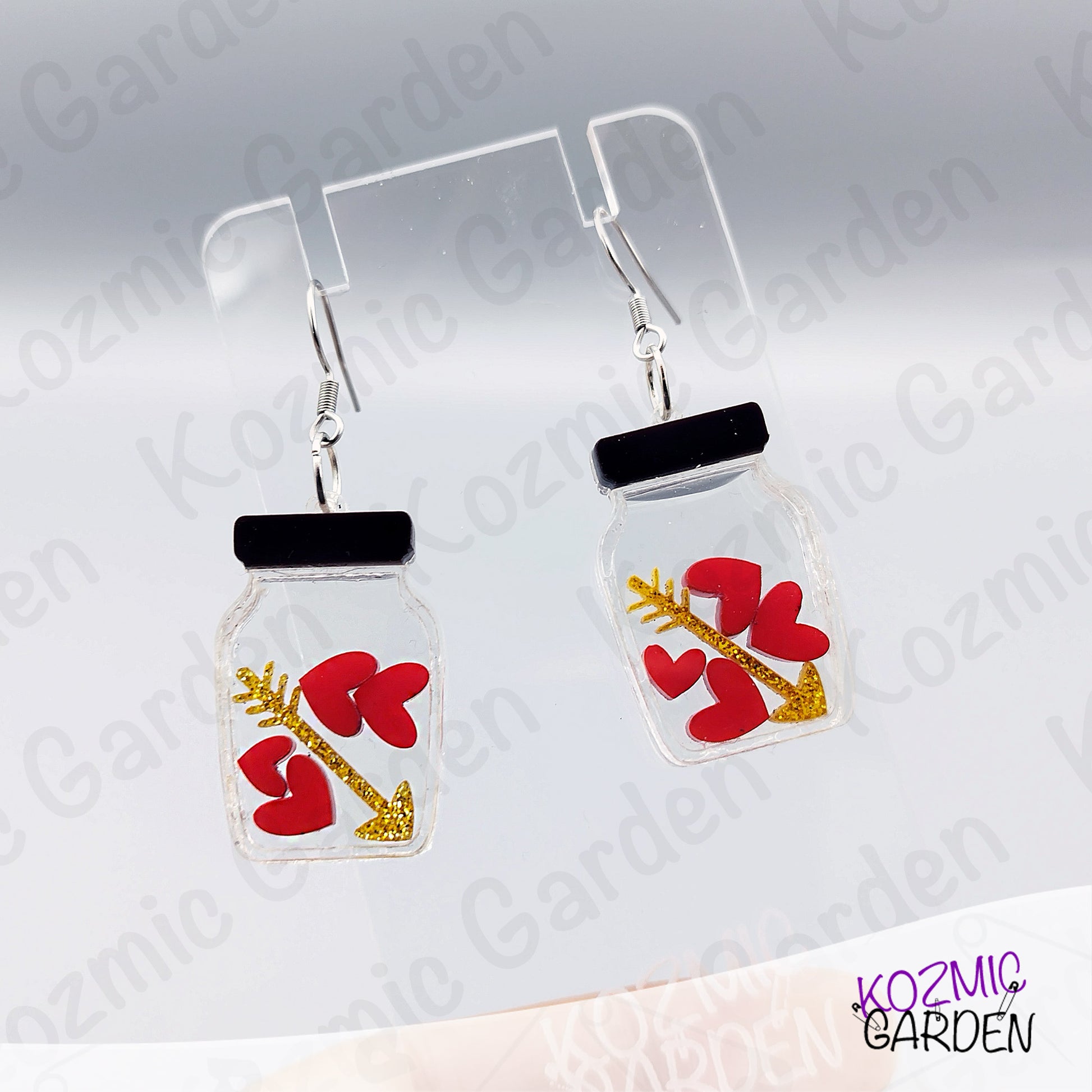 Jar-shaped earrings with red heart and arrow design on a gray background, branded 'Kozmic Garden'.