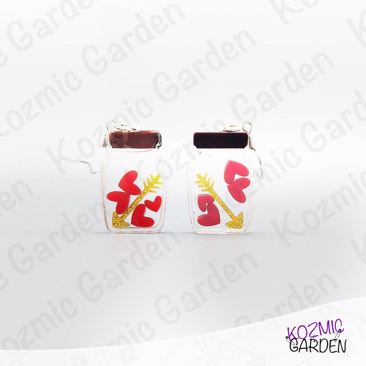 Pair of earrings with red heart and gold arrow design on a white background with 'Kozmic Garden' branding.