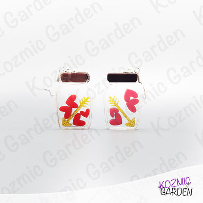 Pair of earrings with red heart and gold arrow design on a white background with 'Kozmic Garden' branding.