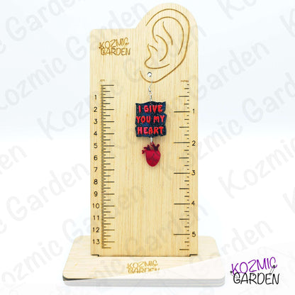 Wooden ear gauge with heart-shaped pendant and ruler on a white background, branded 'Kozmic Garden'.