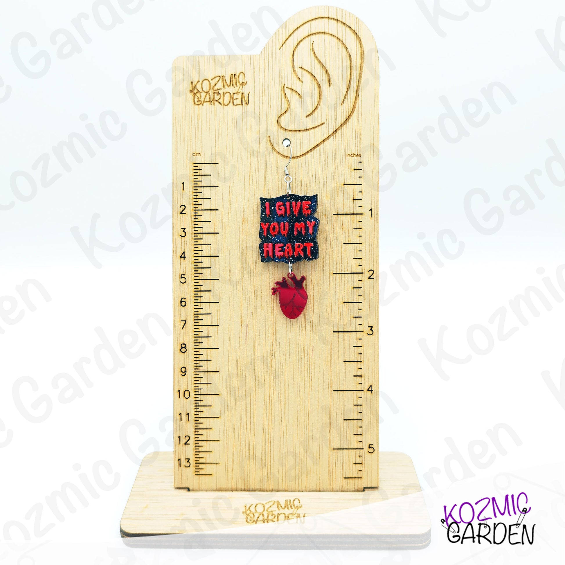 Wooden ear gauge with heart-shaped pendant and ruler on a white background, branded 'Kozmic Garden'.