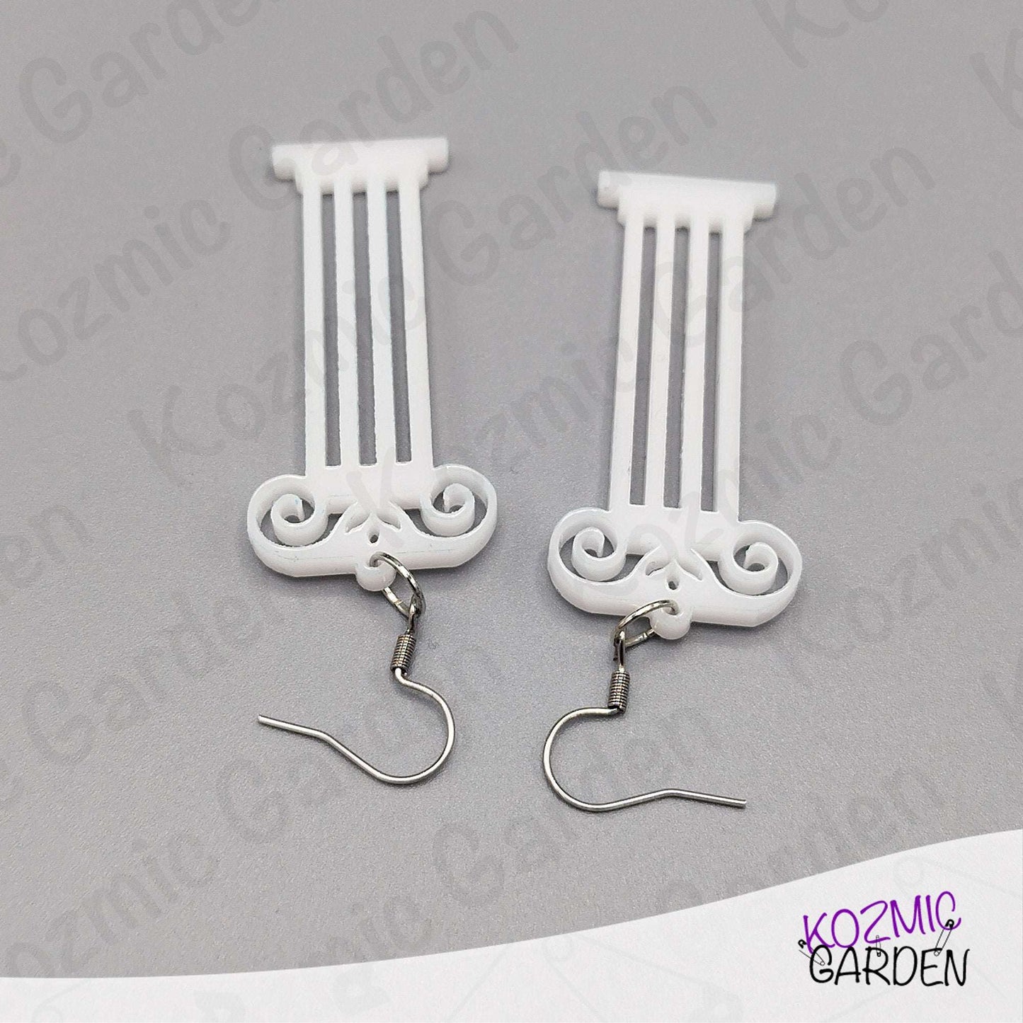 White decorative earrings with intricate designs on a gray background, branded 'Kozmic Garden'.