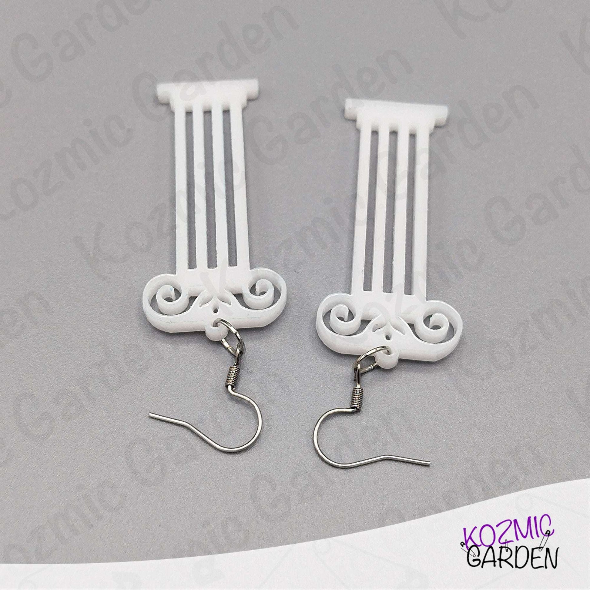 White decorative earrings with intricate designs on a gray background, branded 'Kozmic Garden'.