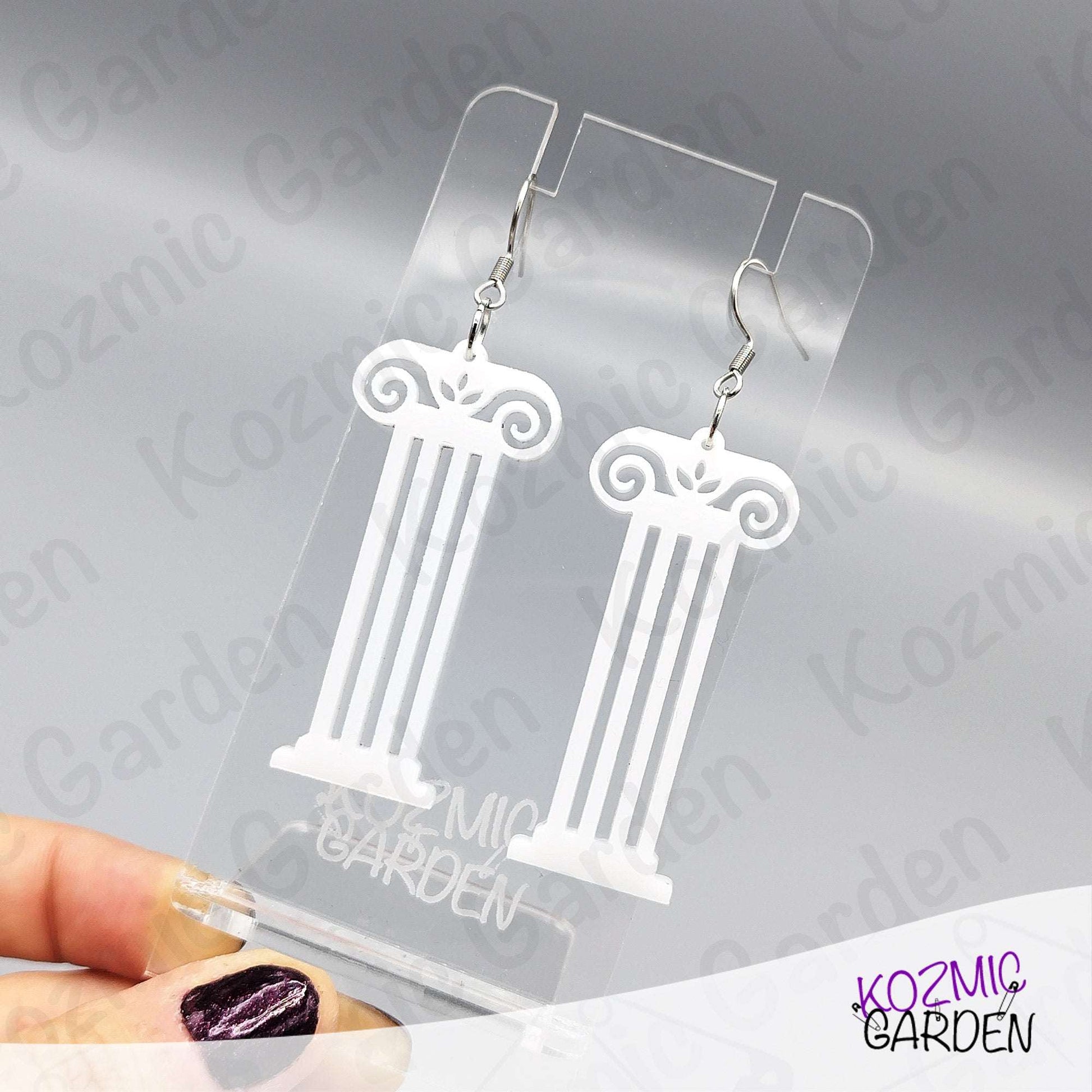 White column-shaped earrings on a clear Kozmic Garden display card.