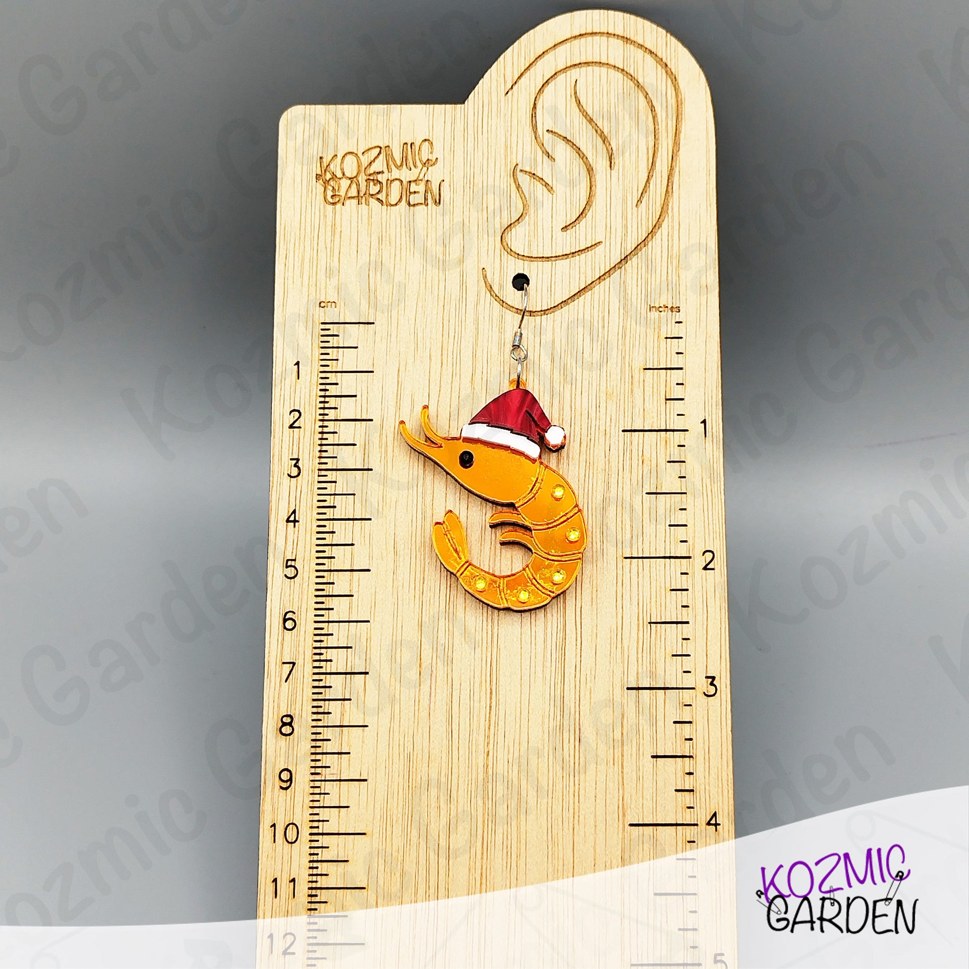 Wooden ruler with a shrimp ornament wearing a Santa hat on a gray background, branded 'Kozmic Garden'.