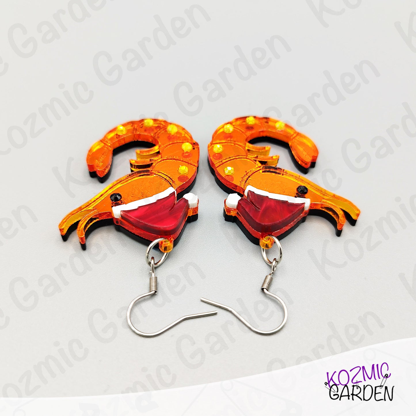 Shrimp-shaped earrings with orange and red design on a white background with 'Kozmic Garden' branding.