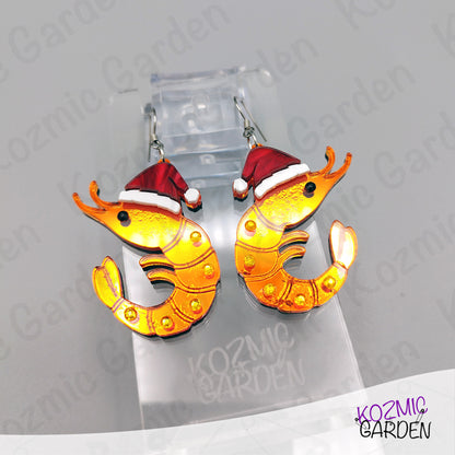Shrimp-shaped earrings with Santa hats on a Kozmic Garden branded stand.