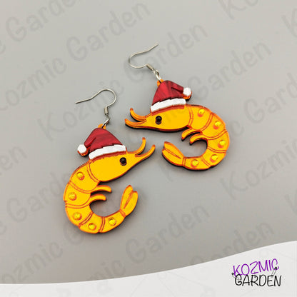Shrimp-shaped earrings with Santa hats on a gray background, branded 'Kozmic Garden'.