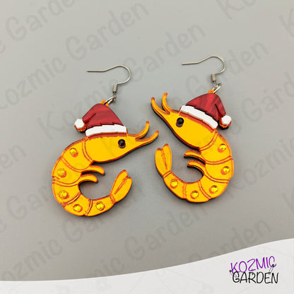 Shrimp-shaped earrings with Santa hats on a gray background, branded 'Kozmic Garden'.