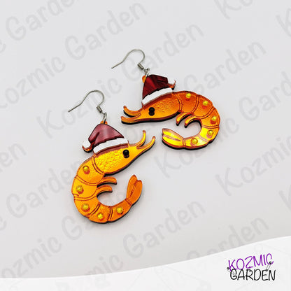 Shrimp-shaped earrings with Santa hats on a white background with 'Kozmic Garden' branding.