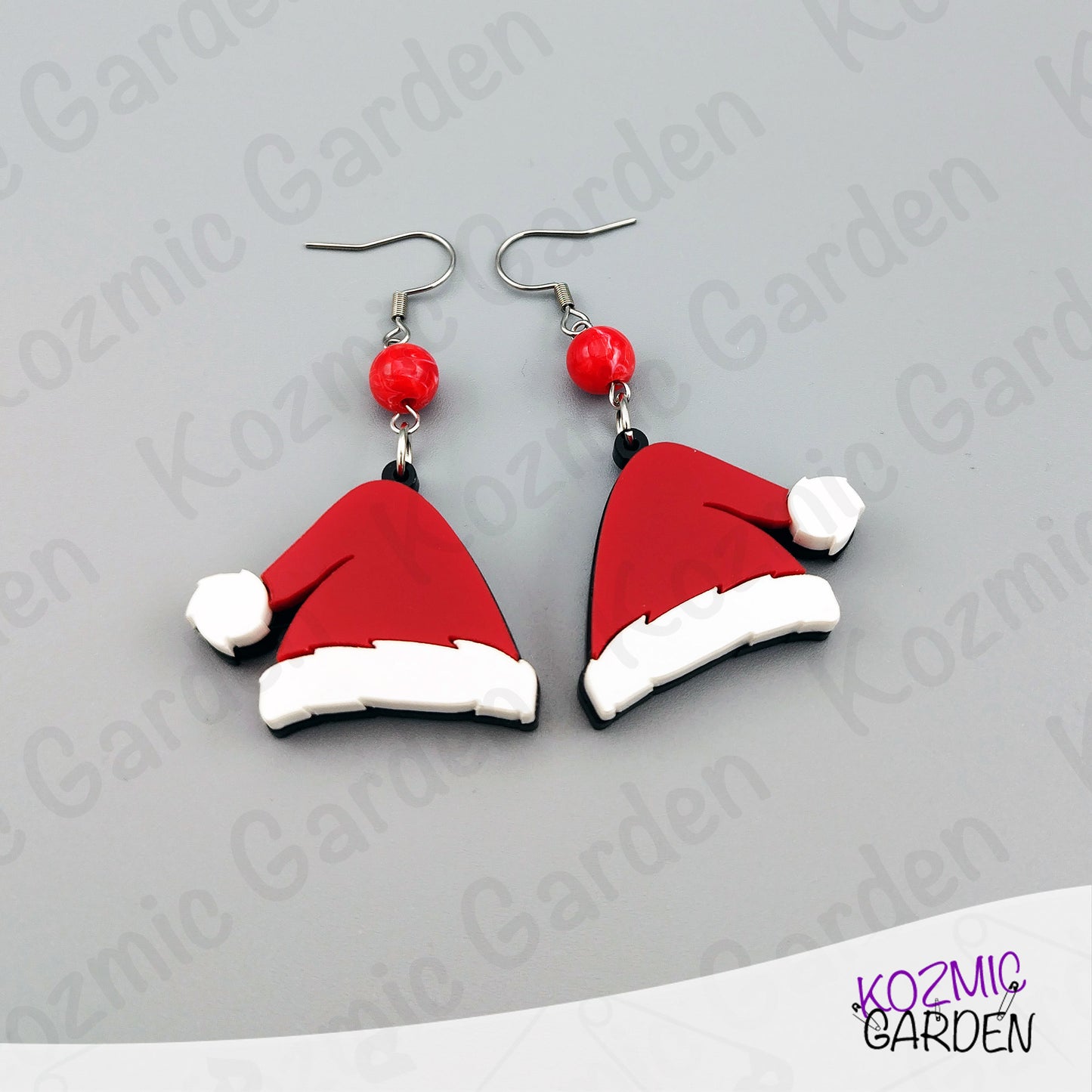Santa hat earrings with red beads on a gray background, branded 'Kozmic Garden'.