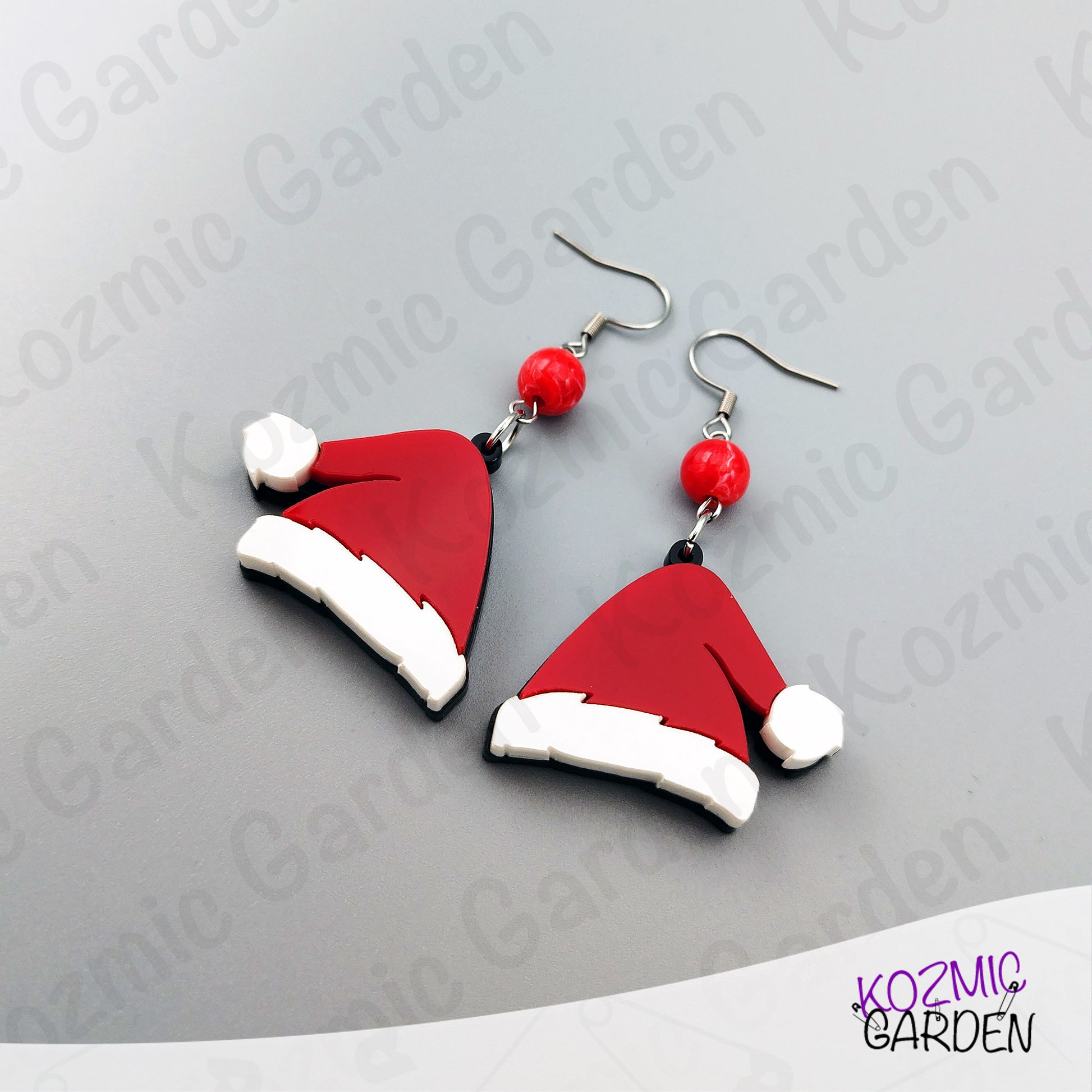 Santa hat earrings with red beads on a gray background, branded 'Kozmic Garden'.