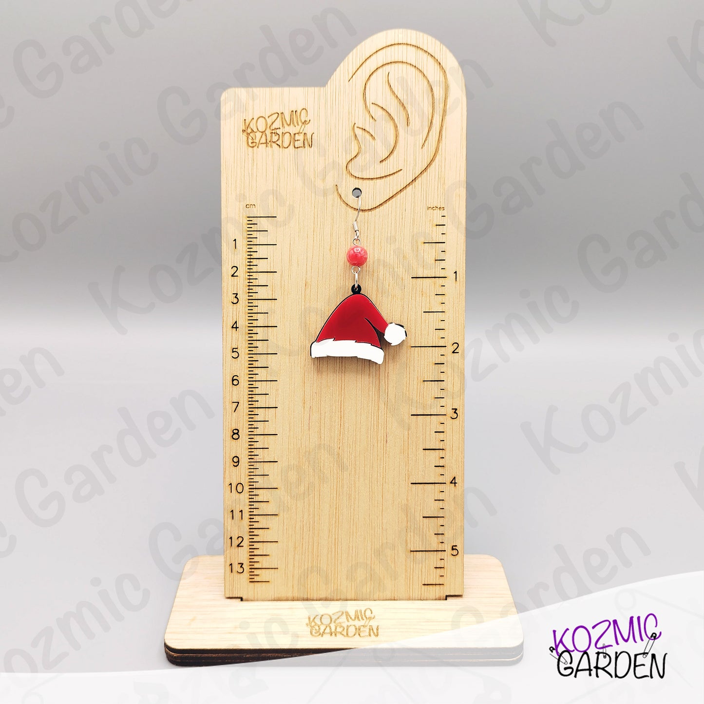 Wooden ear gauge with a Santa hat earring on a gray background, branded 'Kozmic Garden'.